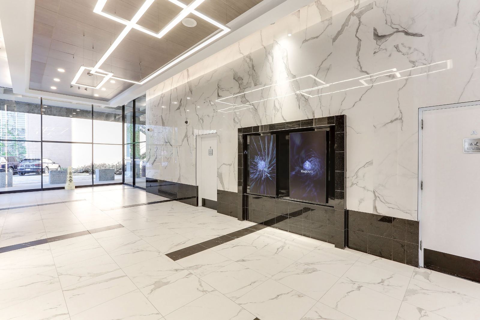 Twin digital directory screens recessed into a black polished tile alcove within the marble-look porcelain wall, lit by a linear LED reveal above and flanked by a flush service door.