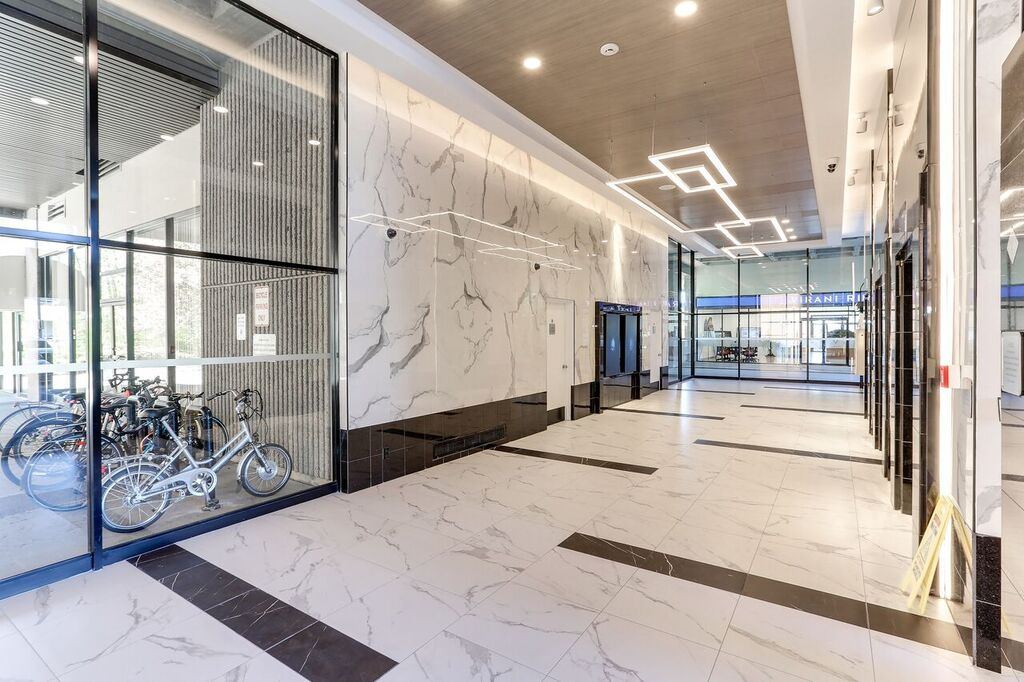 Close perspective of the book-matched marble-look porcelain wall running above a black tile base, with the new white marble-pattern floor tile and its black inset banding sweeping past the glazed bicycle storage room.